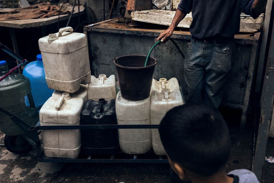 People line up to fill buckets with water from a nearby stream in El Cementerio, a slum in western Caracas.