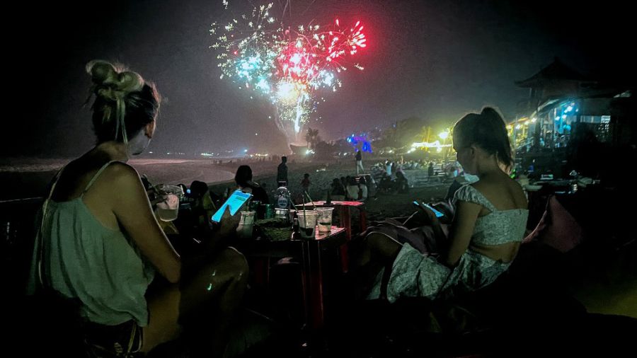 Una playa en Indonesia, con gente festejando Año Nuevo y los fuegos artificiales de fondo.