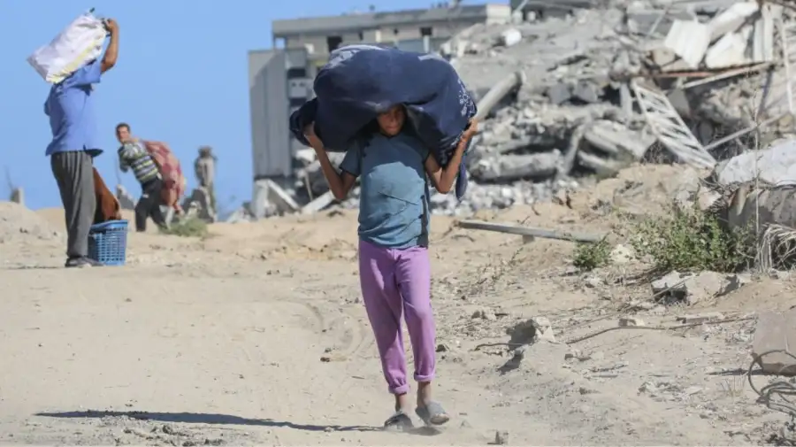 Un niño con sus pertenencias regresa a sus hogar en la zona de Al Zahra