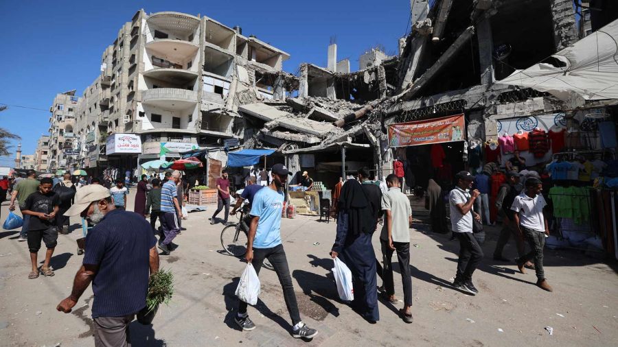 Fotogaleria Palestinos caminan junto a un edificio destruido en un mercado improvisado en el campo de refugiados de Nuseirat, ubicado en el centro de la Franja de Gaza, tres días después de la entrada en vigor del alto el fuego