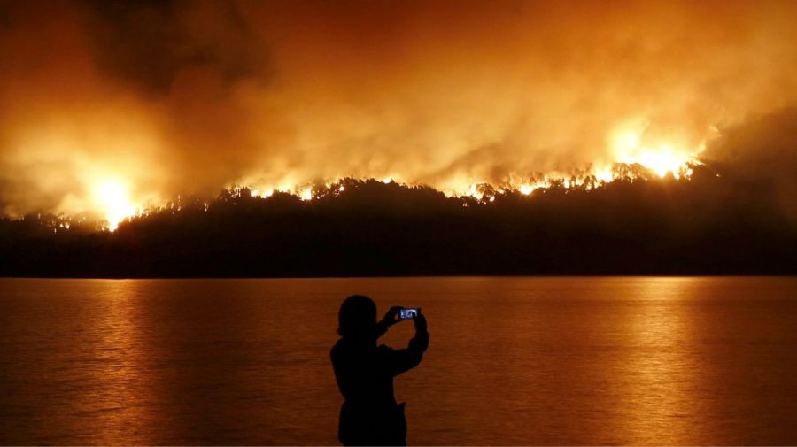 Una mujer toma fotografías mientras el fuego consume el parque nacional Los Alerces, en Chubut