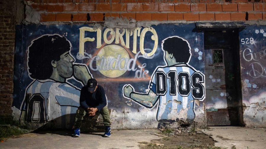 Fotogaleria Un hombre se sienta frente a un mural que representa al fallecido astro del fútbol Diego Maradona y lee en español Fiorito, ciudad de Dios en el patio de la casa de la infancia del fallecido futbolista