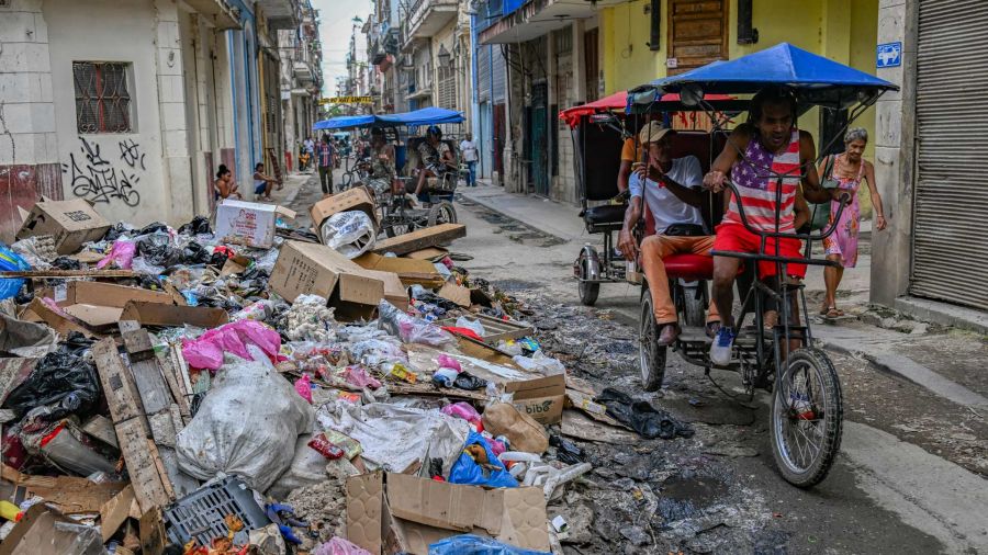 Fotogaleria Una persona con una camiseta con la bandera de Estados Unidos pasa en triciclo junto a un montón de basura en una calle de La Habana, Cuba