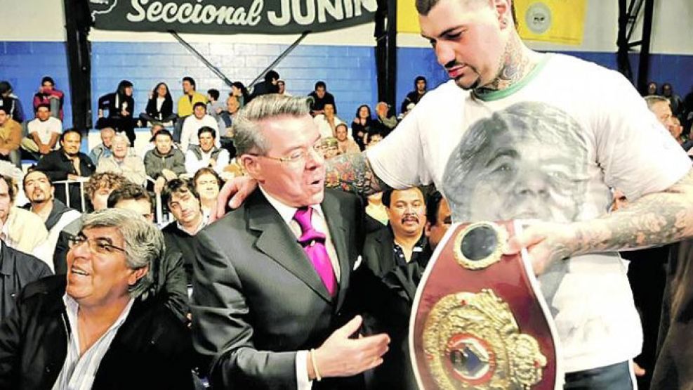 El "Patón" Basile le muestra orgulloso el cinturón de ganador al juez federal Norberto Oyarbide. A su lado, un sonriente Hugo Moyano.