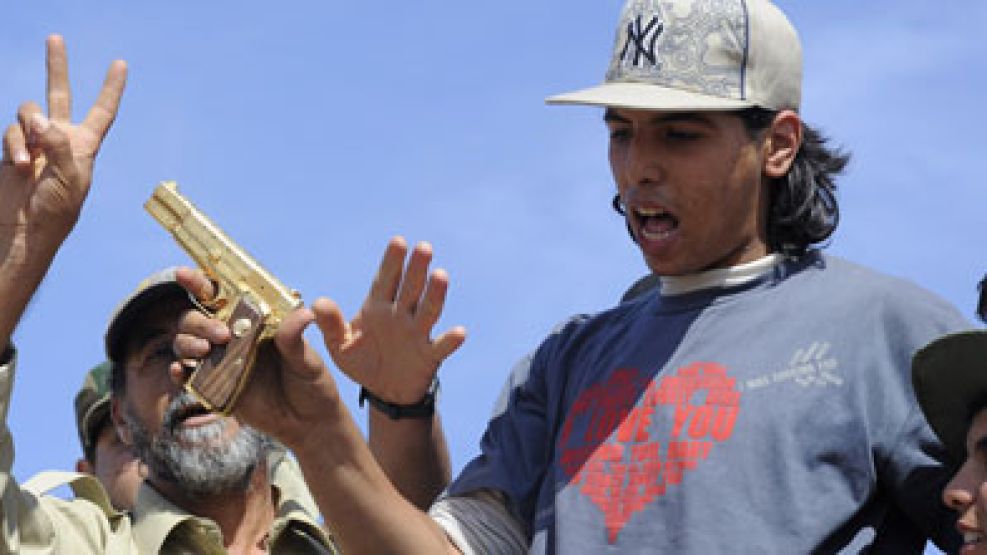 El joven muestra la pistola 9mm dorada que pertenecía a Kadafi.