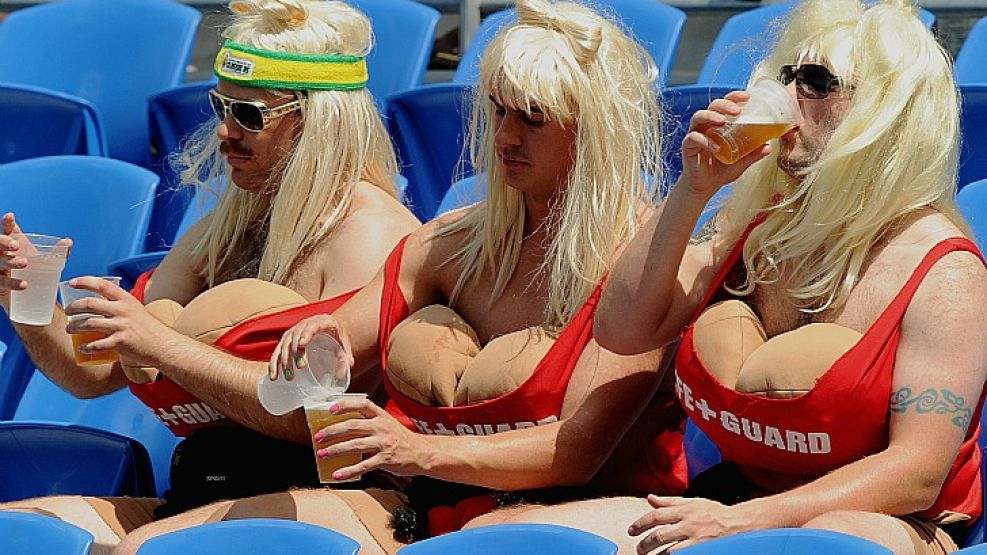 Tres hombres disfrazados de mujer disfrutan de un refresco durante un partido de rugby en el circuito mundial de seven.