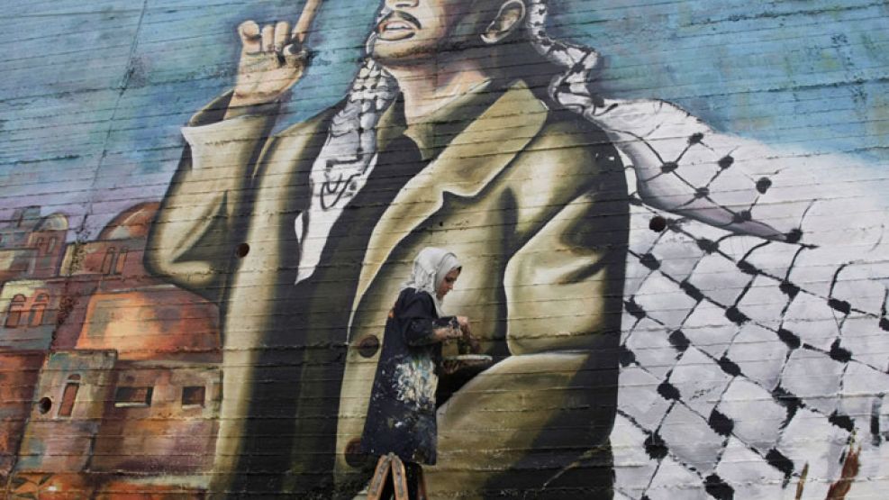 Recuerdo. Una mujer palestina camina delante de la imagen de Yasser Arafat en Cisjordania.