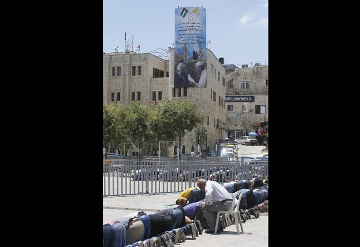 Adoradores musulmanes palestinos asisten al rezo semanal de los viernes al lado de un cartel gigante del líder palestino Mahmud Abbas y el Papa Francisco.