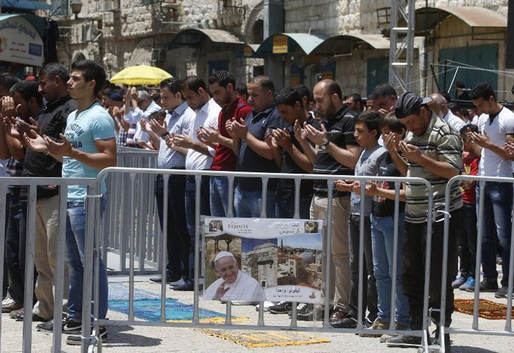 Adoradores musulmanes palestinos asisten al rezo semanal de los viernes al lado de un una cerca que lleva un cartel con la foto del Papa Francisco.