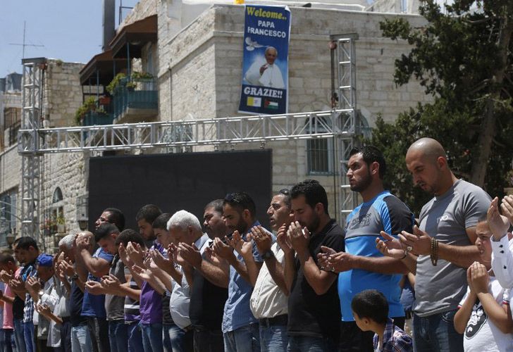 Adoradores musulmanes palestinos asisten al rezo semanal de los viernes al lado de un cartel que lleva un retrato del Papa Francisco.