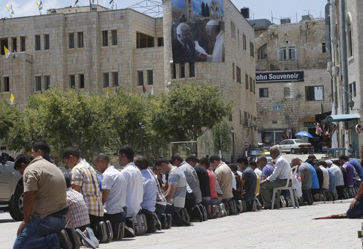 Adoradores musulmanes palestinos asisten al rezo semanal de los viernes al lado de un cartel gigante del líder palestino Mahmud Abbas y el Papa Francisco.