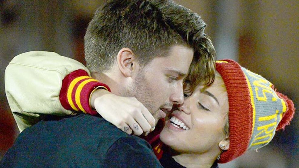 Selfie. Celular en mano para registrar el beso, Patrick Schwarzenegger con Miley Cyrus sobre él. Besos en un estadio deportivo.