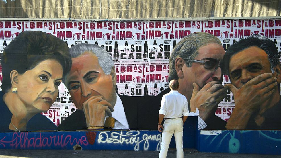 En Brasilia, una persona observa un mural en el que Eduardo Cunha habla con Dilma Rousseff. Al mismo tiempo, el titular de la Cámara de Diputados conspira con Aecio Neves.
