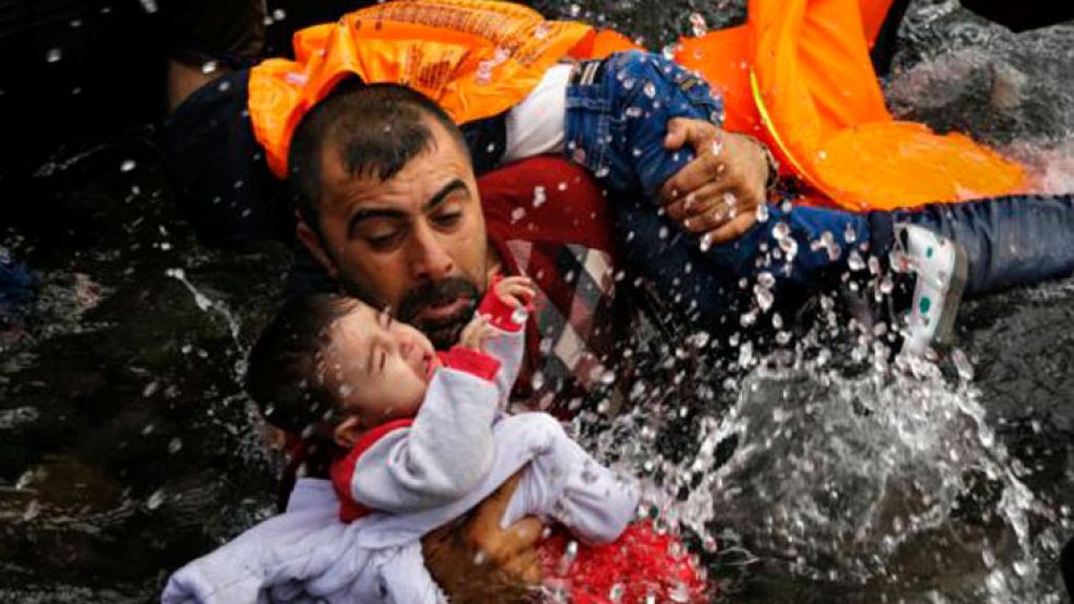 Un refugiado sirio sujeta a su hijo mientras lucha por salir de su bote en la isla griega de Lesbos. 