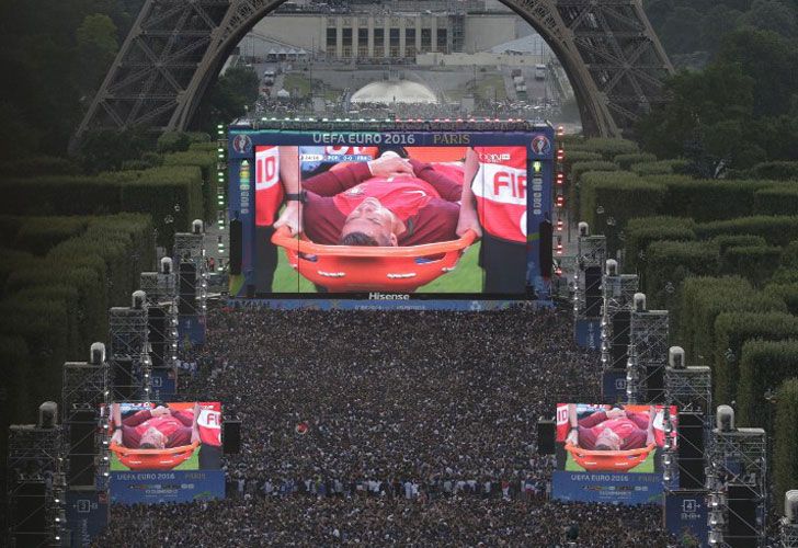 La gente ve en una pantalla gigante el torneo de fútbol Euro 2016 entre Portugal y Francia, mientras que el delantero portugués Cristiano Ronaldo es evacuado en una camilla después de ser herido, el 10 de julio de 2016 en la zona de los fanáticos de los Campos de Marte cerca de la Torre Eiffel en París.