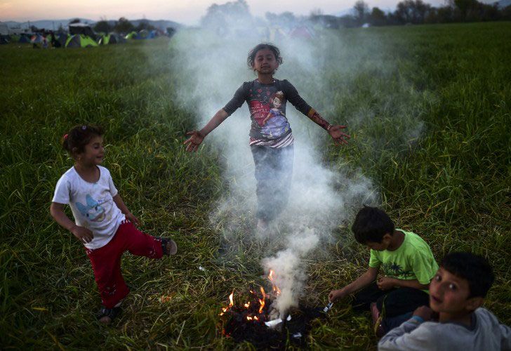 Los niños se reúnen alrededor de una fogata en el campamento improvisado de la frontera entre Grecia y Macedonia, cerca del pueblo griego de Idomeni, el 31 de marzo de 2016, donde más de 11.000 refugiados y migrantes están actualmente bloqueados por el bloqueo de la frontera balcánica.