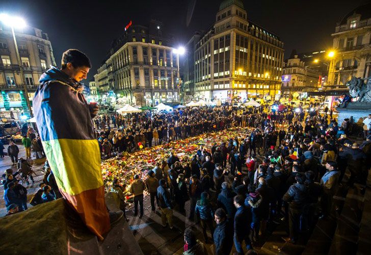 Un hombre envuelto en una bandera belga sostiene una vela mientras que la gente se reúne en un monumento improvisado delante de la bolsa de Bruselas en la plaza de la bolsa (Beursplein) el 24 de marzo de 2016.