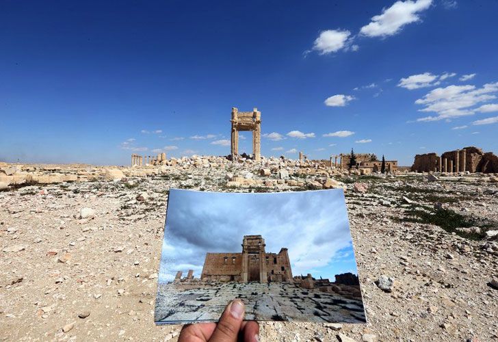 Una visión general tomada el 31 de marzo de 2016 muestra a un fotógrafo que sostiene su cuadro del templo de Bel tomado el 14 de marzo de 2014 delante de los restos del templo histórico después de que fuera destruido por el grupo islámico del estado (IS) jihadists en septiembre de 2015 En la antigua ciudad siria de Palmyra. Las tropas sirias respaldadas por las fuerzas rusas recapturaron Palmyra el 27 de marzo de 2016, después de una feroz ofensiva para rescatar a la ciudad de los yihadistas que ven las magníficas ruinas de la UNESCO como idólatras.