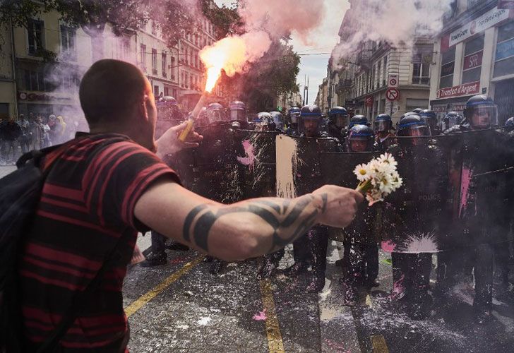 Un hombre sostiene un ramo de flores y una antorcha mientras se enfrenta a la policía antidisturbios durante una manifestación contra la reforma laboral planificada del gobierno, el 26 de mayo de 2016 en Lyon, en el centro-este de Francia.