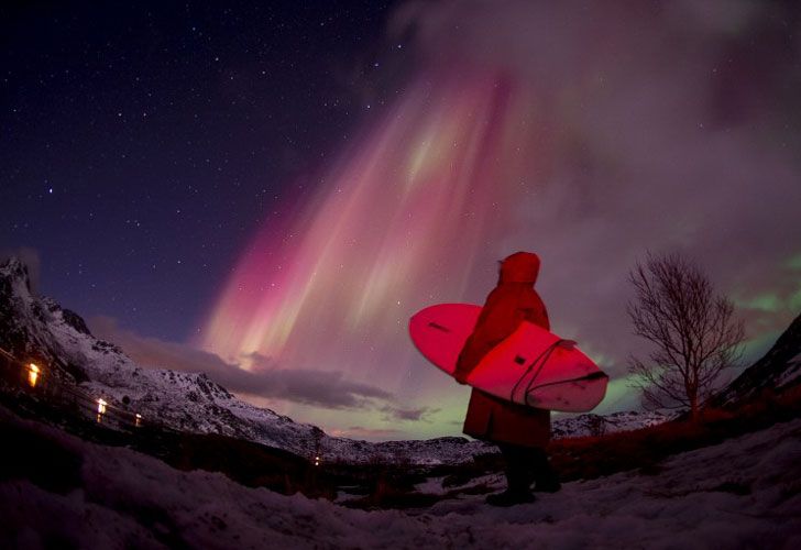 Una persona que practica surf mira las luces norteñas (aurora borealis) que iluminan el cielo sobre la playa nevada de Unstad, en las islas de Lofoten, círculo ártico, el 14 de marzo de 2016.