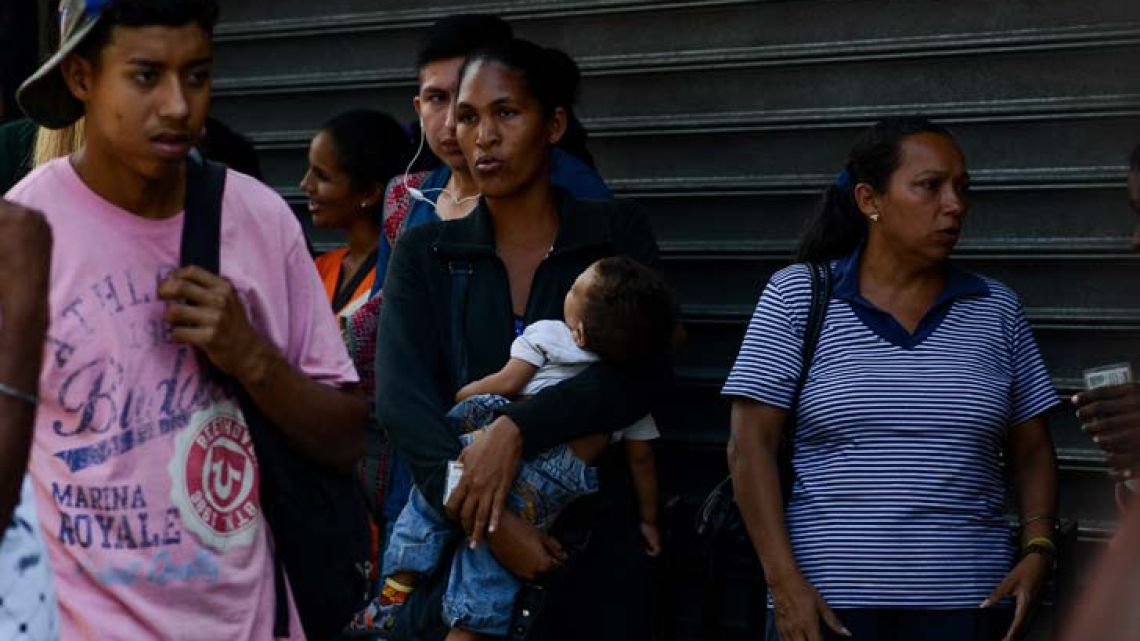 A woman holds her baby while queuing outside a supermarket in Caracas.