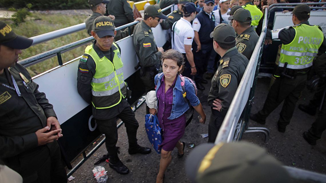 In this July 17, 2016 file photo, police stand guard as a Venezuelan woman crosses into Colombia through the Simon Bolivar bridge linking San Antonio del Tachira, Venezuela, with Cucuta, Colombia.