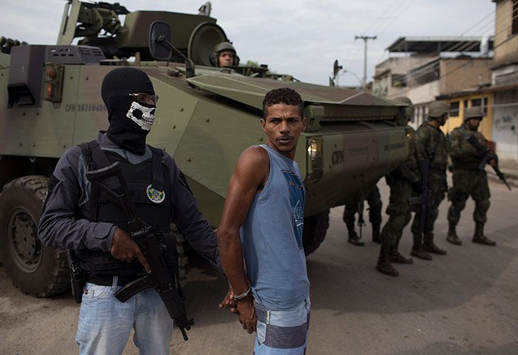 Un oficial de policía enmascarado junto a un sospechoso esposado durante una operación sorpresa en el barrio pobre de Kelson en Río de Janeiro, Brasil