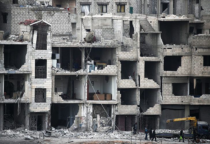 Sirios pasan frente a los edificios destruidos en Arbin en el enclave de los rebeldes de Ghouta Oriental