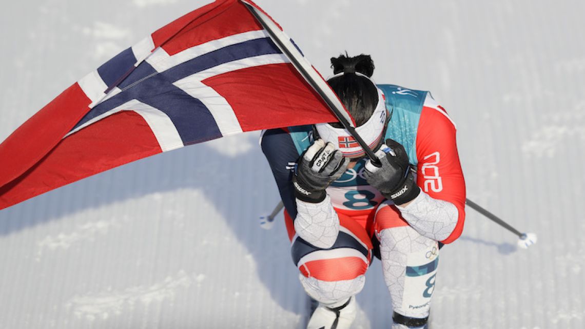 Norway's Marit Bjoergen carries her country's flag after winning gold in the women's 30k cross-country skiing competition at the 2018 Winter Olympics