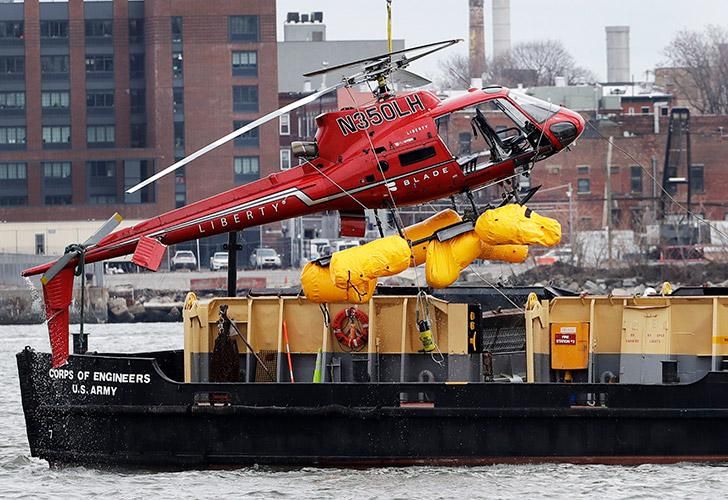 Un helicóptero es levantado por una grúa desde el East River hacia una barcaza.