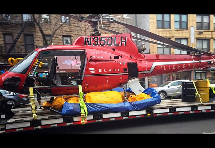 Un helicóptero es levantado por una grúa desde el East River hacia una barcaza.