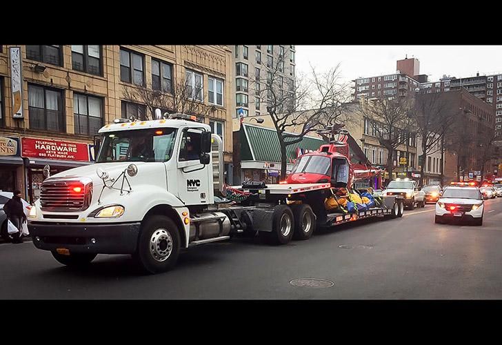 Un helicóptero que se estrelló en el East River de Nueva York matando a cinco pasajeros es transportado en un camión remolque con una escolta policial, a lo largo de Flatbush Avenue en Brooklyn Borough of New York