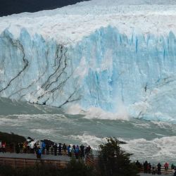 Tourists watch pieces of ice falling from the Perito Moreno glacier, at Parque Nacional Los Glaciares near El Calafate, in the province of Santa Cruz, on March 12, 2018.