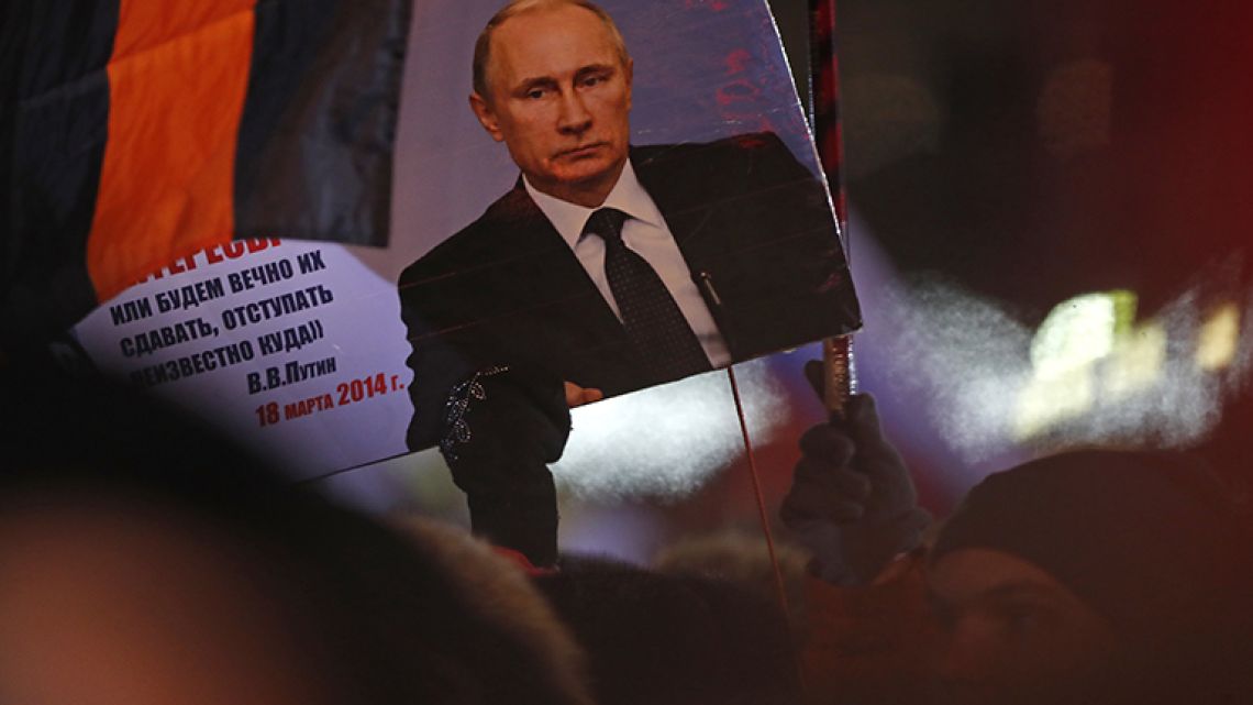 A person holds a banner of Russian President Vladimir Putin in Manezhnaya square, near Kremlin in Moscow, Sunday, March 18, 2018.