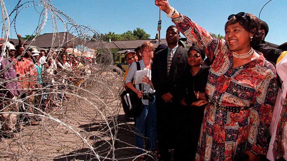 Winnie Madikizela-Mandela, former wife of Nelson Mandela, greets demonstrators, behind razor wire at a bail hearing for businessman Piet Odendaal in Viljoenskroon, South Africa in November 2000.