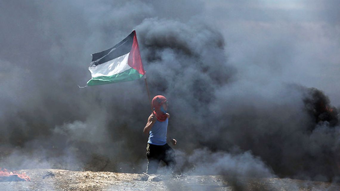 A boy waves a Palestinian flag while walking through black smoke from burning tires during a protest on the Gaza Strip's border with Israel, Monday, May 14, 2018. Thousands of Palestinians are protesting near Gaza's border with Israel, as Israel prepared for the festive inauguration of a new US Embassy in contested Jerusalem.