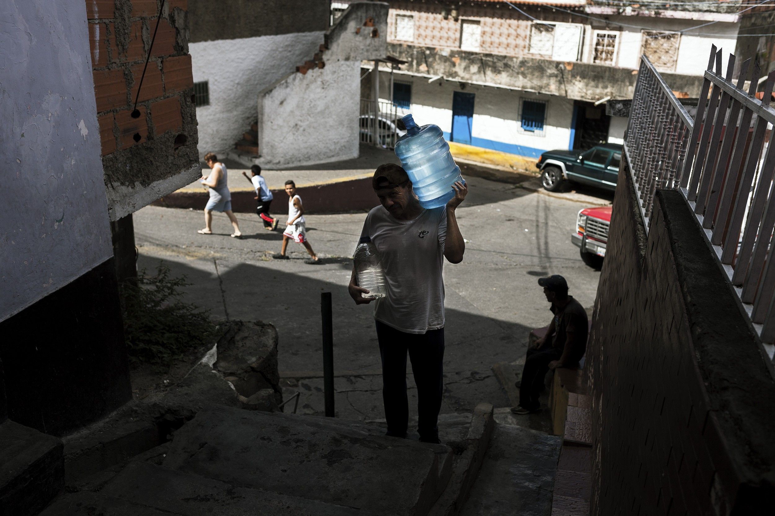 A man carries 5 gallons of water up a steep flight of stairs. For the elder, the water crisis has hit the hardest: Some have to walk for miles to find a water source and carry gallons of water uphill.