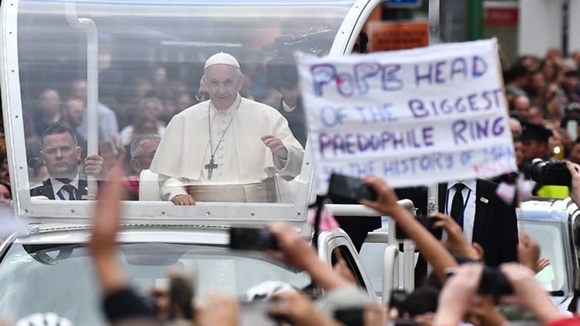 Pope Francis waves to the faithful on his popemobile in Dublin on Saturday, during his visit to Ireland to attend the 2018 World Meeting of Families. A protester's sign – addressing child sex abuse and paedophilia in the Catholic Church – can be seen in the foreground of the image. 