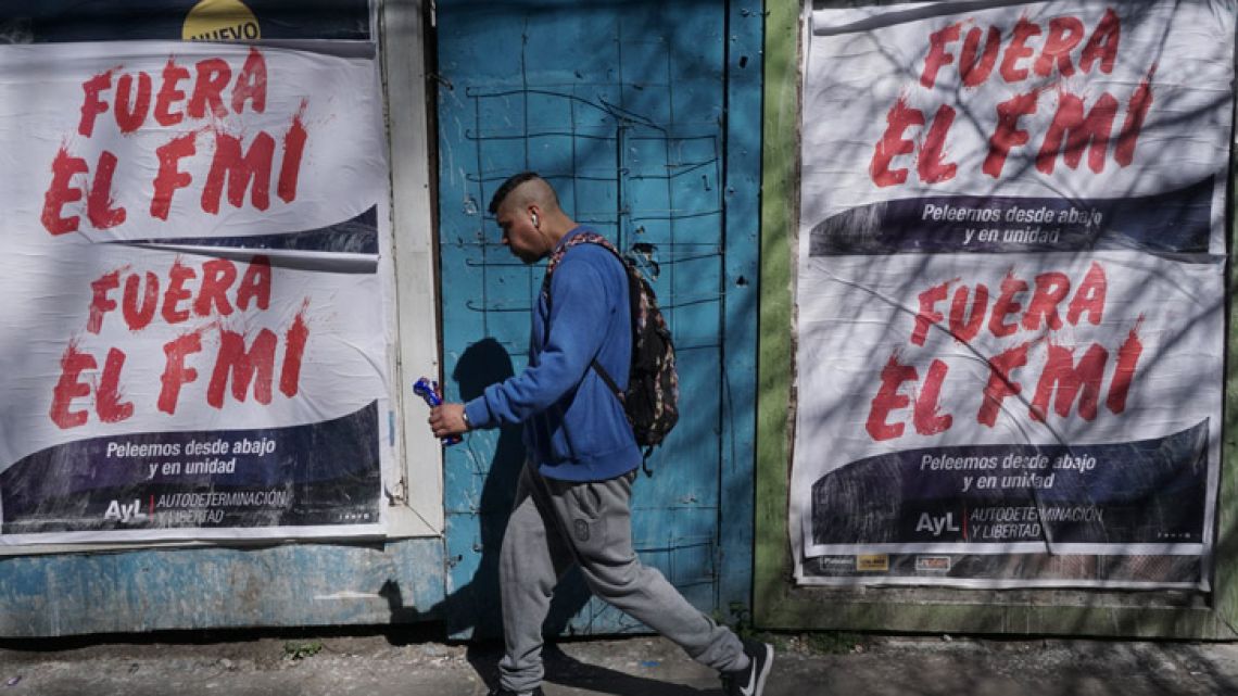 A man walks past posters rejecting the government's negotiations with the International Monetary Fund (IMF).