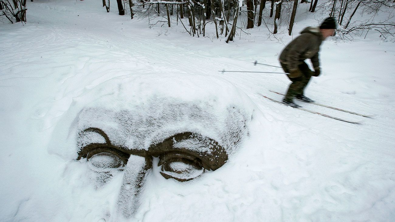 Un hombre pasa junto a una enorme cabeza nevada tallada en piedra y enterrada en el suelo en el parque Sergievka, en las afueras de San Petersburgo, Rusia.