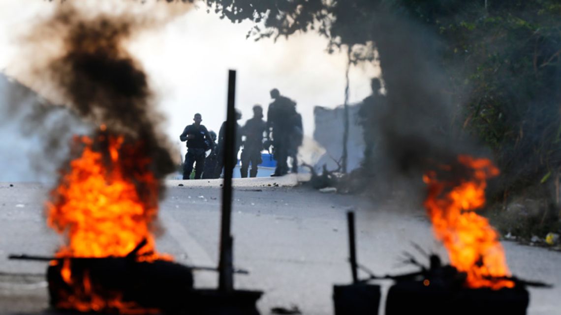 Bolívarian National Police stand behind a burning roadblock set up by anti-government protesters who are showing support for a mutiny by some National Guard soldiers in the Cotiza neighbourhood of Caracas.