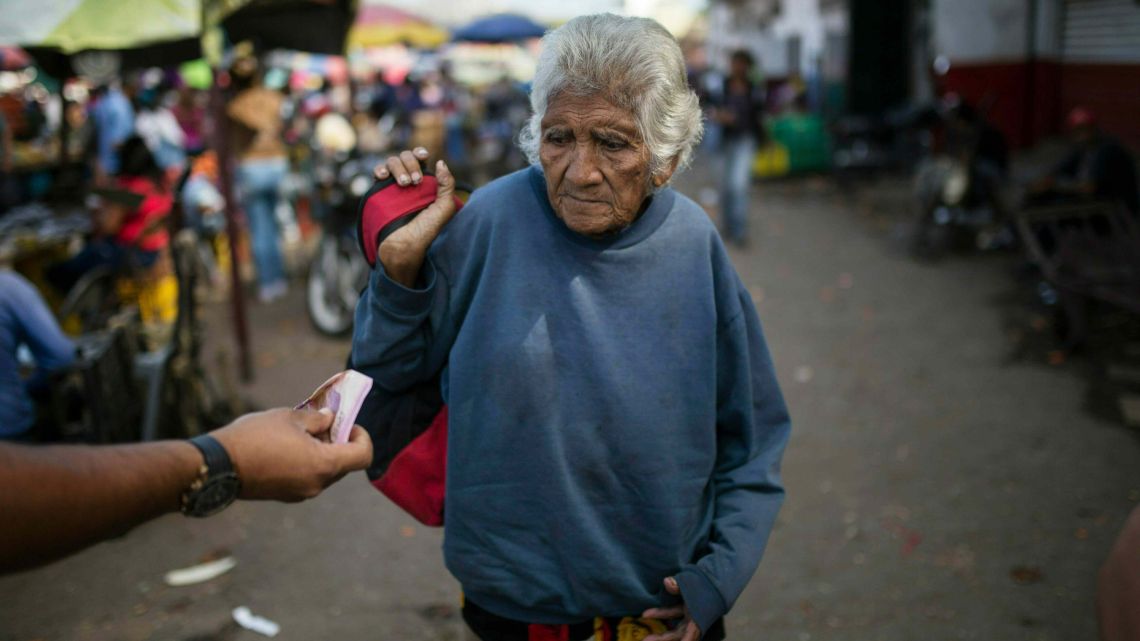A woman is offered cash as she begs at a wholesale food market in Caracas, Venezuela on Monday