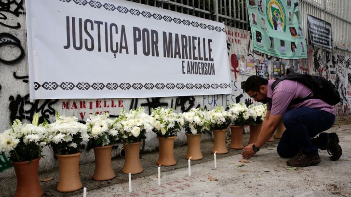 During a presentation marking the one year anniversary of the death of Rio Councilwoman Marielle Franco, in Rio de Janeiro, Brazil, a man lights a candle in front of a row of flowers to commemorate her death. 