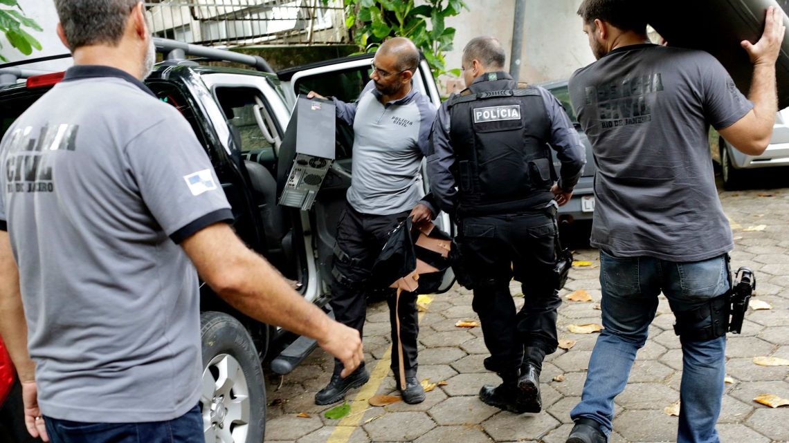Civil police officers carry a computer and other items confiscated from the home of the suspects in the killing of councilwoman Marielle Franco. The brazen assassination on March 14 last year led to massive protests and widespread anger throughout Brazil