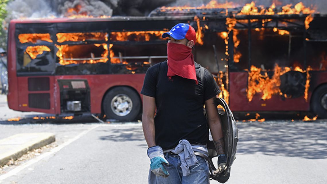 An opposition demonstrator walks near a bus in flames during clashes with soldiers loyal to Venezuelan President Nicolás Maduro, after some troops joined opposition leader Juan Guaidó in his campaign to oust Maduro's government, in the surroundings of La Carlota military base in Caracas on April 30, 2019.