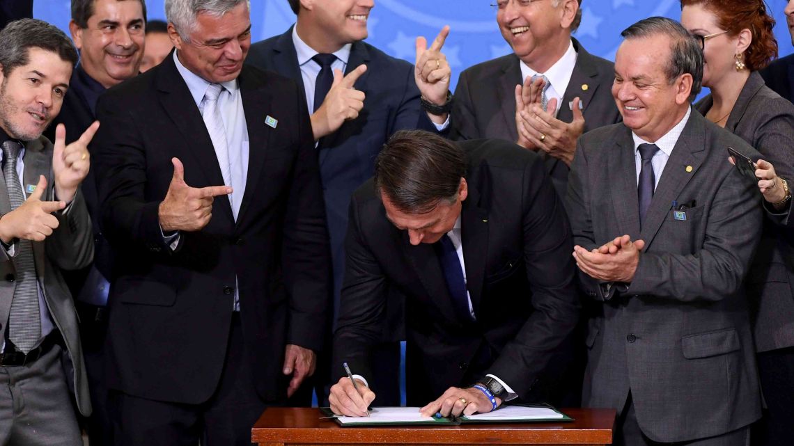 Brazilian President Jair Bolsonaro (C) signs the decree that facilitates to own, carry and import weapons surrounded by parliamentarians during a ceremony at the Planalto Palace in Brasilia, on May 7, 2019. 