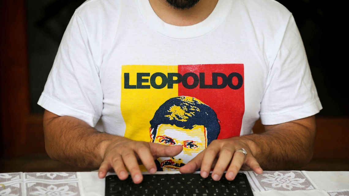 In this Saturday, May 11, 2019 photo, wearing a T-shirt featuring Leopoldo López, Venezuelan opposition leader Freddy Guevara, exiled at the Chilean ambassador's residence, types on a computer keyboard in Caracas, Venezuela. Guevara, in his first televised interview since taking refuge in the lush diplomatic compound 18 months ago, said as foreign embassies in Caracas fill up with dissidents the world will be forced to take notice of how Nicolás Maduro's clinging to power is not only inflicting more damage on what's left of the rule of law in Venezuela but spilling over its borders as well.