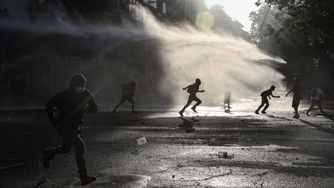 Anti-government protesters run amid the spray of a police water cannon during demonstrations against economic inequality in Santiago.