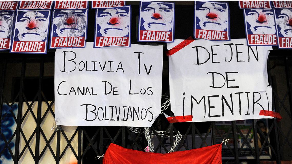 View of the closed entrance of the state TV channel BoliviaTV with pictures depicting Bolivian President Evo Morales as a clown reading "Fraud" and signs reading "Bolivia TV channel of Bolivians" and "Stop lying" next to a Bolivian national flag, after a protest on November 9, 2019, in La Paz. 