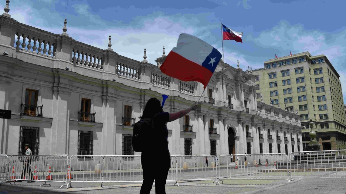 A demonstrator flutters a Chilean national flag outside La Moneda presidential palace in Santiago, on the fourth week of protests against the government of Chilean President Sebastián Piñera on November 11, 2019.